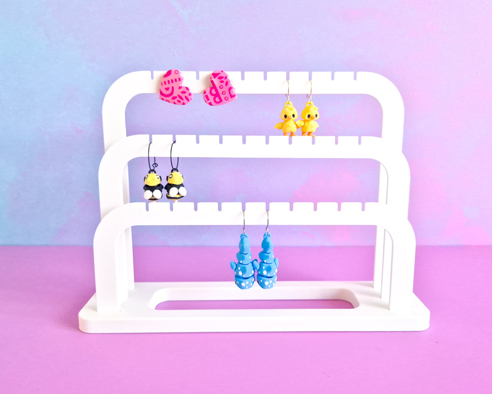 White tiered earring stand with colorful earrings on a pastel gradient background