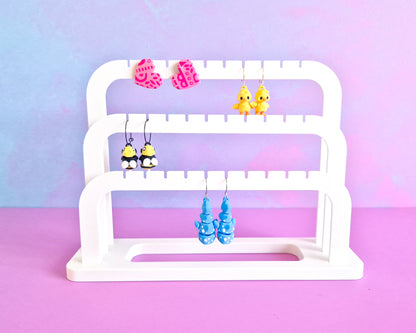 White tiered earring stand with colorful earrings on a pastel gradient background